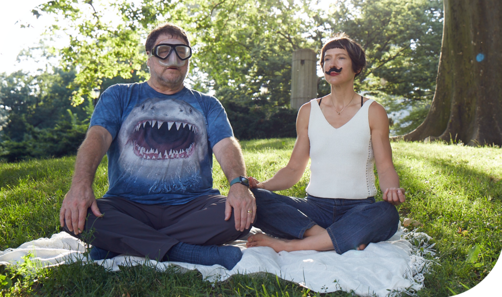 Mark wearing a shark t-short and scuba mask, Alia wearing a mustache, both sitting in meditation poses